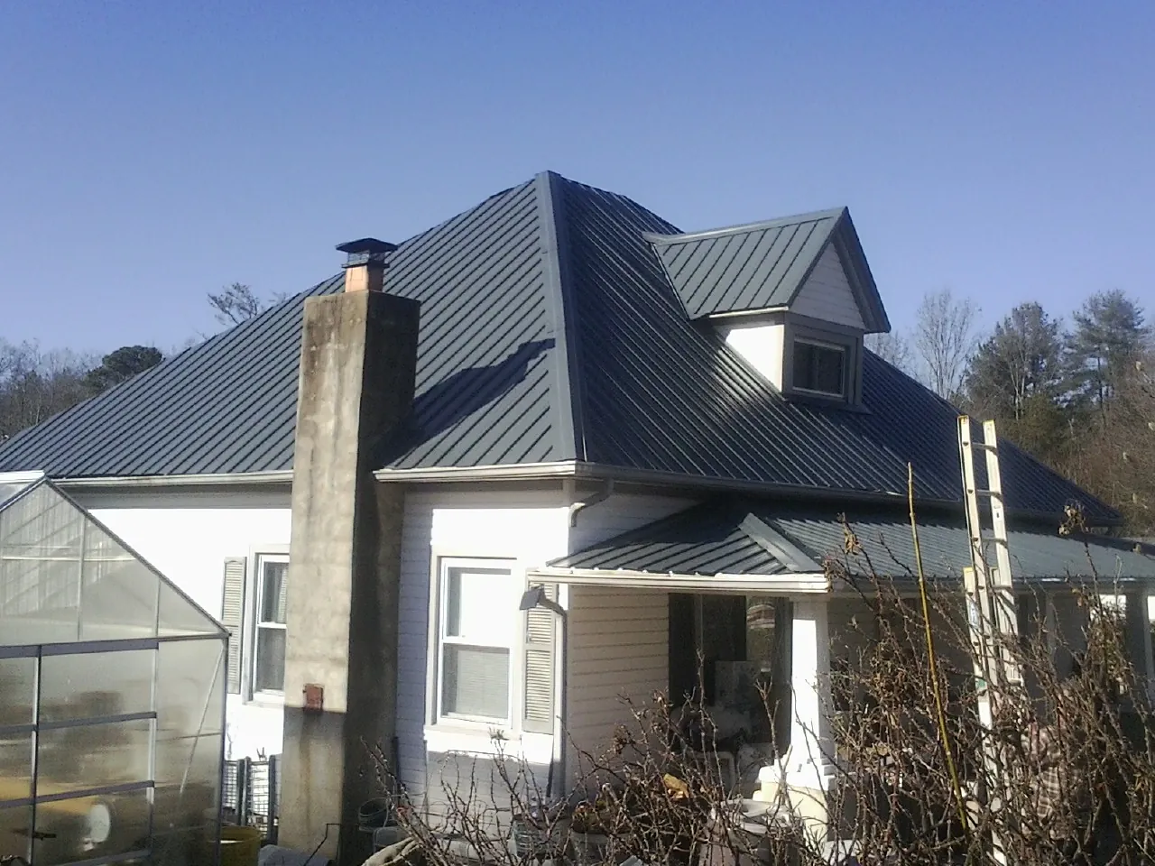 Dark blue standing seam metal roof on a white farmhouse with dormer — Slate & Tile Roof Repair by Roofing Brothers in New Ipswich