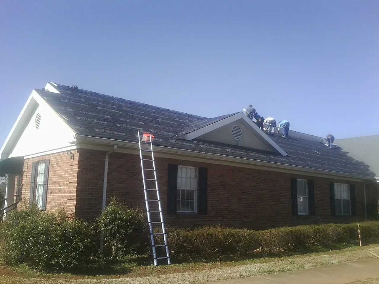 Crew tearing shingles off a brick ranch roof with a ladder set — Metal Roof Repair work by our crew in New Ipswich
