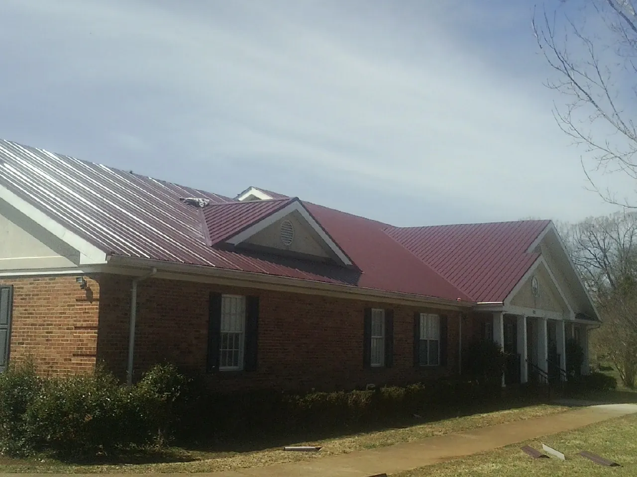 Red metal roof with gabled entries on a long brick building, from a Hail Damage Roof Repair job in New Ipswich