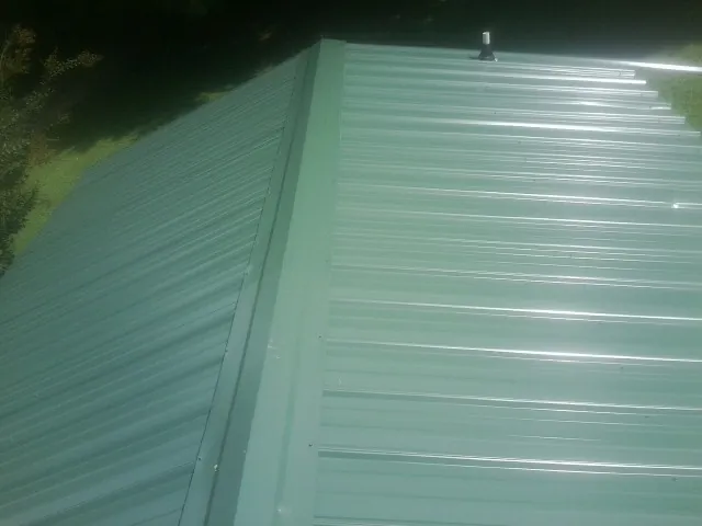 New green metal panels meeting at the ridge of a roof — Flat Roof Repair work by our crew in New Ipswich