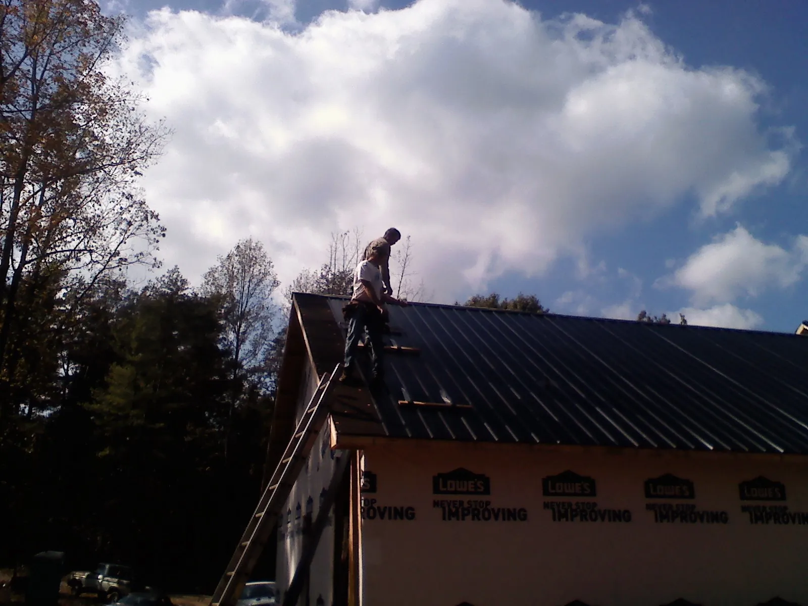 Roofer fastening dark metal panels high against a cloudy sky, from a Roof Inspection job in New Ipswich