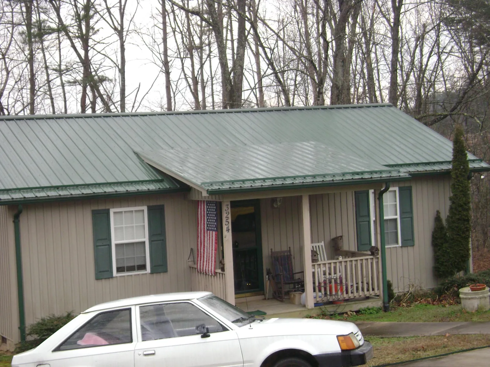 Green metal roof and front porch on a tan sided cottage in New Ipswich