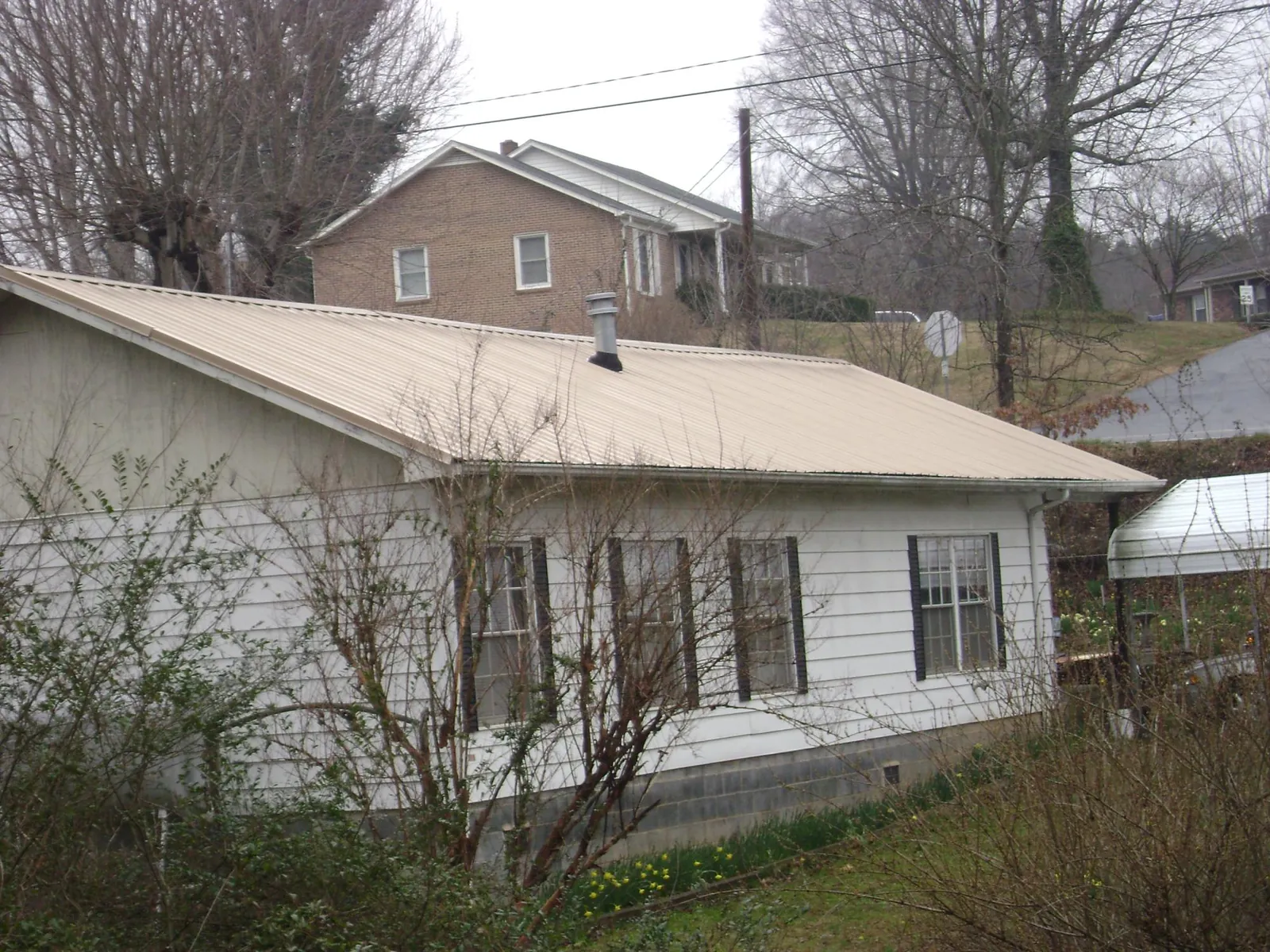 Tan metal roof on a white sided house set into a hillside — Commercial Roofing by Roofing Brothers in New Ipswich